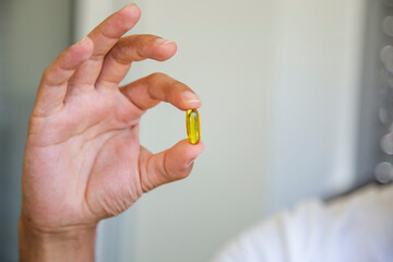 Close-up of person's hand holding Omega3 fish oil capsule against white background