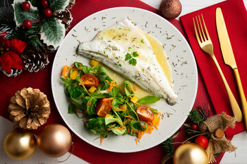 Baked sea bass with lemon sauce. Top view table with christmas decorations.