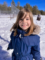 Smiling child outdoors in a snowy park with pine trees and blue sky