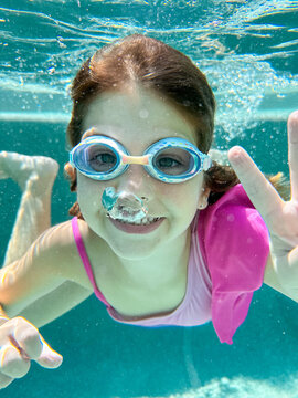 Smiling girl underwater, wearing goggles, making a peace sign