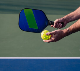 Close up of hand holding pickleball paddle and ball on outdoor court.