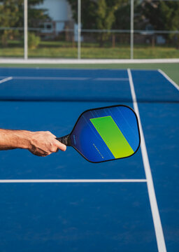 Close up of hand holding pickleball paddle on blue outdoor court.