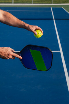 Close up of hand holding pickleball paddle and ball on outdoor court.