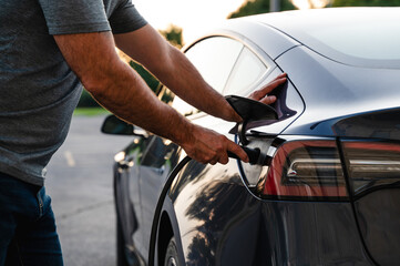 Close up of man plugging EV charger into electric vehicle outside.