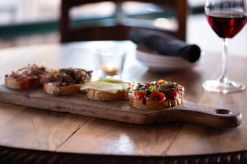 A bruschetta board sitting a wood table with a glass of wine