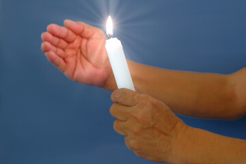 Two hands holding lighted candle to cover from blowing wind