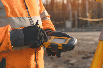 Construction worker conducting measurements with  handheld device in an outdoor setting during sunset © Iryna