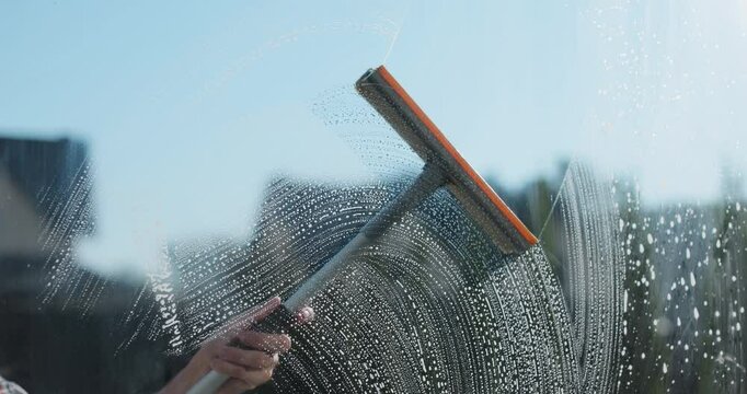Woman hands wipes with a scraper dirty window close up. Washes a window, glass with a brush. Concentration of cleanliness, cleaning companies.