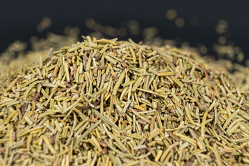 Pile of chopped dry rosemary seasoning on a black background.