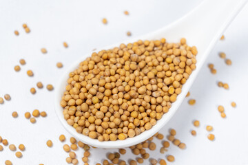 Mustard seeds in a spoon, white background, natural organic seasoning