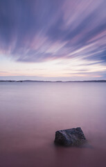Long exposure captures a serene stone amidst the calming waters of Sweden at twilight