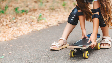 Obraz premium Active child girl in casual wear practicing skateboard tricks on street embracing her penny board in the park looking away with charming smile