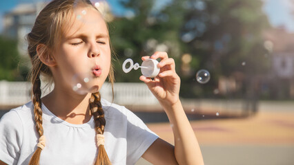 Girl blowing soap bubbles in summer day in the park