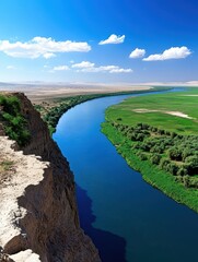 Obraz premium Scenic River Winding Through a Lush Valley Under a Blue Sky