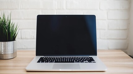Fototapeta premium A sleek laptop sits on a wooden desk, surrounded by a small potted plant against a white brick wall.