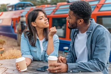 Casual coffee conversation between a young couple by colorful boats at a vibrant riverside location