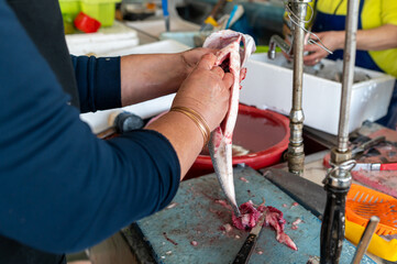 Fish being cleaned at a bustling market with vendors and fresh seafood during daytime