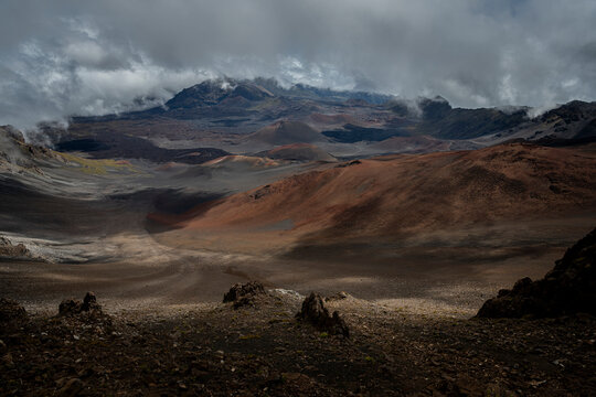 View of red and brown Haleakala Crater with fog and cloud cover