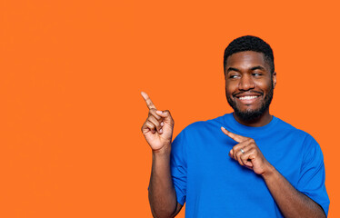 A cheerful young man in a blue shirt playfully gestures pointing towards empty place an orange...