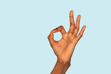 A hand displaying the okay gesture against a soft blue background, symbolizing positivity and...