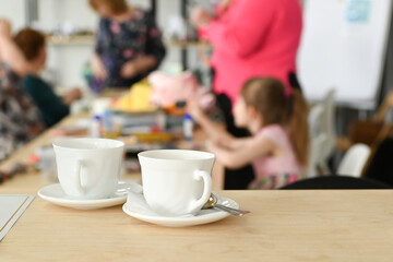 Two white tea cups on a wooden table with blurred background of unrecognizable people in a meeting