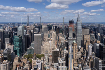Aerial view of Manhattan skyline with numerous skyscrapers under a blue sky with scattered clouds.