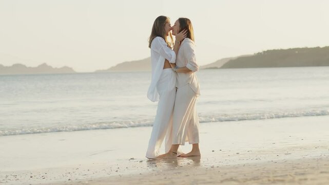 Romantic young lesbian couple kissing on a beach at sunset