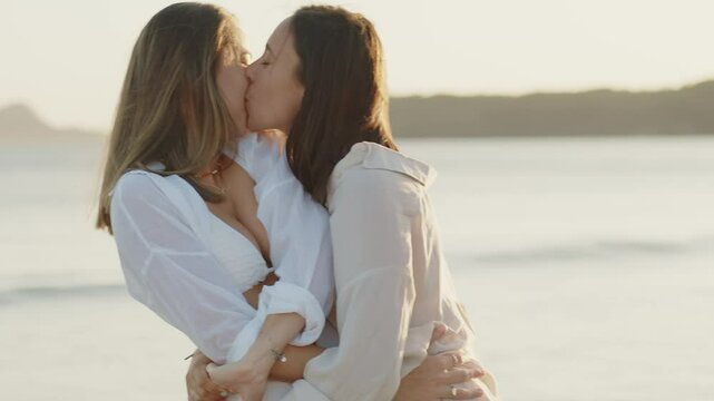 Young lesbian couple kissing romantically on a beach at sunset