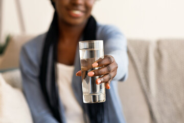 Healthcare Concept. Friendly African American Girl Holding Glass of Mineral Water Offering it On Camera, Selective Focus