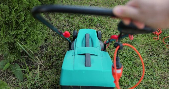 Man cuts the grass on the lawn with an electric lawnmower.
