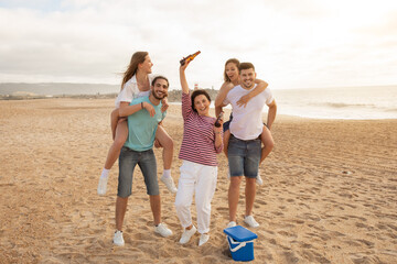 A family enjoys a fun beach day, with two members giving piggyback rides while others celebrate...