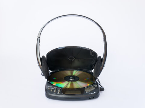Close-up view of CD player with open lid and golden CD inside and headphones isolated on white background