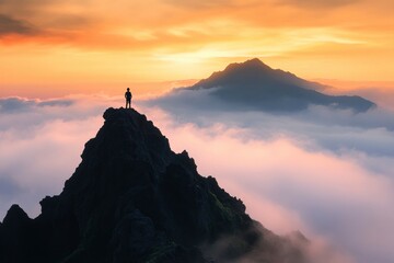 A person stands on a mountain peak, looking out over a misty landscape