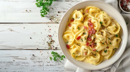 tortellini in creamy cheese sauce with crispy bacon in white bowl on white wood table landscape view from above