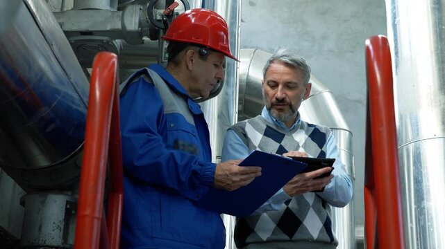 Technical Manager Giving Instructions to Worker With Clipboard in Industrial Interior with Large Piping. Supervisor Controls the Work of an Employee in District Heating Plant. People at Work.