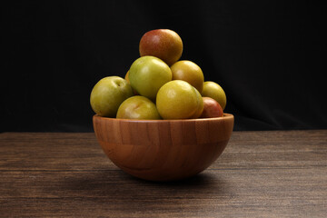 Ripe sweet small mini plum green maroon on rustic wooden table bowl black background