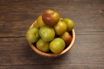 Ripe sweet small mini plum green maroon on rustic wooden table bowl black background