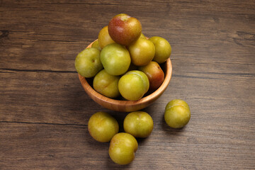 Ripe sweet small mini plum green maroon on rustic wooden table bowl black background
