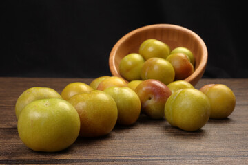 Ripe sweet small mini plum green maroon on rustic wooden table bowl black background