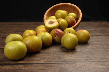 Ripe sweet small mini plum green maroon on rustic wooden table bowl black background