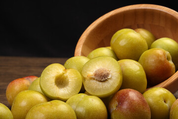 Ripe sweet small mini plum green maroon on rustic wooden table bowl black background