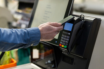 Person makes contactless payment using smartphone at store checkout. Technology enables convenient...