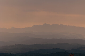 colline che si estendono fino alle montagne lontane, in un ambiente naturale lungo il confine tra l'Italia e la Slovenia, coperte dalla pioggia, dalle nuvole e dalla foschia, di sera, al tramonto