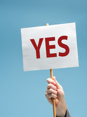 Male hand holding sign with the word YES  against a blue background