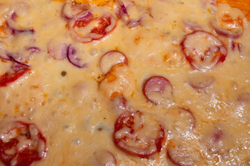 Pizza close-up. Top view of the surface of the finished pizza with sausages, tomatoes and onions in cheese. Appetizing natural culinary background