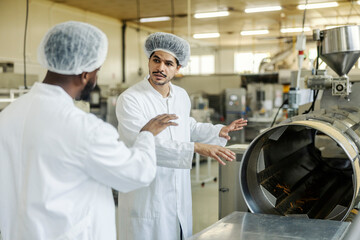 Multicultural production line operator standing near machine and discussing with his supervisor at...