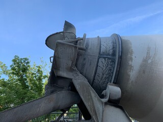 Vertical shot of the back part of  concrete truck. Concrete mixer truck at a construction site. Delivery of concrete for pouring foundations and building structures. White cement mixer in a blue sky.