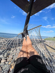 Person legs gently swaying in a hammock on Baltic Sea beach under the bright summer sun