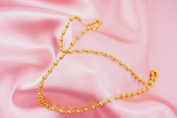 A Gold Necklace on pink color silk background.