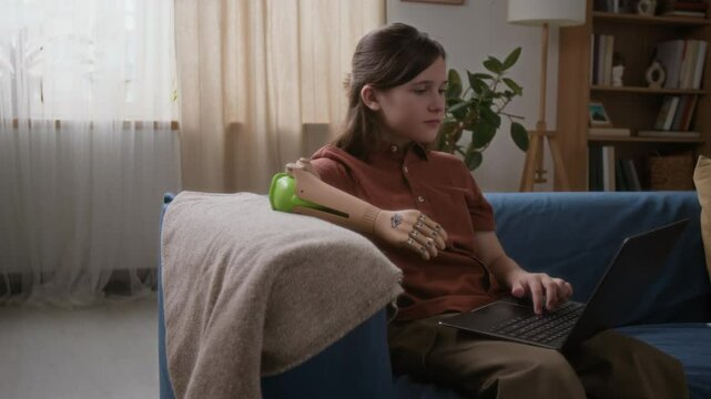Teenage girl with disability studying on laptop online in living room